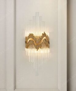 chiếc đèn gắn tường với thiết kế là những ống thuỷ tinh trong suốt được cố định chắc chắn vào tường bằng những thanh dồng mã vàng ốp tường, một sự kết hợp sang trọng và tinh tế