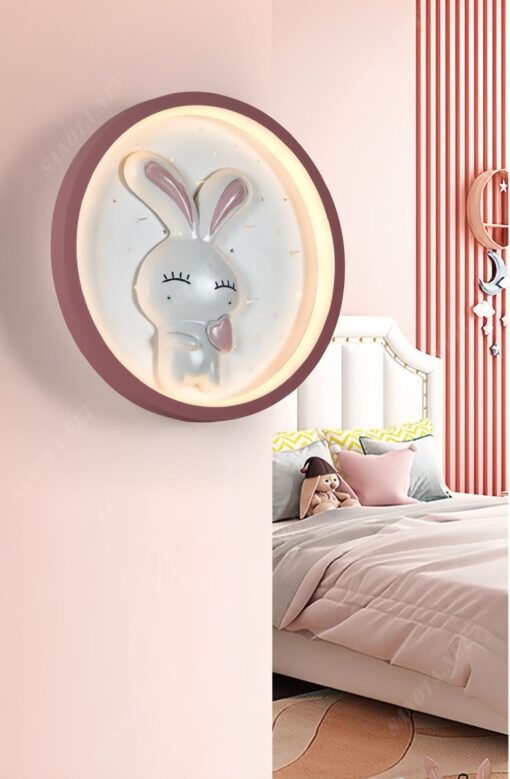 một chiếc đèn gắn tường là một mâm đèn led tròn có thiết kế chú thỏ trắng ở bênn trong vòng tròn kết hợp với đường viền màu hồng, một chiếc đèn phù hợp cho căn phòng của bé gái dễ thương đáng yêu