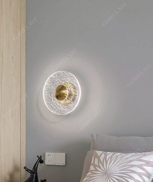 một chiếc đèn gắn tường với thiết kế hiện đại và sang trọng là một mâm đèn led có viền ngoài làm từ chất liệu thuỷ tinh trong suốt có nhưng vân đá độc đáo, chính giữa là điểm nhấn đồng mạ vàng được thiết kế để chiếc đèn có thể được gắn cố định chắc chắn trên tường, đây sẽ là một chiếc đèn phù hợp cho mọi không gian nội thất đặc biệt là phòng ngủ bởi ánh sáng dịu nhẹ và ấm áp mà nó đem lại
