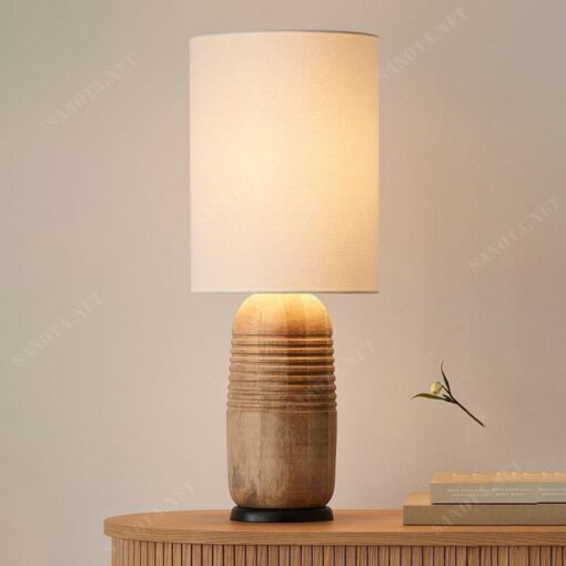 một chiếc đèn để bàn với thân gỗ trụ tròn kết hợp với chao vải, chiếc đèn là sự kết hợp hài hoà của nét đẹp hiện đại, với chao vải ánh sáng ra từ chiếc đèn mềm mại ấm áp