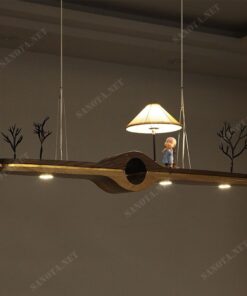 một chiếc đèn thả trần gỗ với thiết kế hiện đại và độc đáo sự kết hợp của gỗ và đèn LED. Một thanh gỗ nằm ngang mộc mạc đơn giản nhưng với điểm nhấn là hình ảnh của tiểu cảnh và chú tiểu, một điểm nhấn dễ thương sẽ giúp cho không gian trang trí chiếc đèn thêm phần nổi bật, đây không chi là một chiếc đèn thả đem lại ánh sáng chất lượng còn là món đồ trang trí cho không gian nội thất căn nhà của bạn