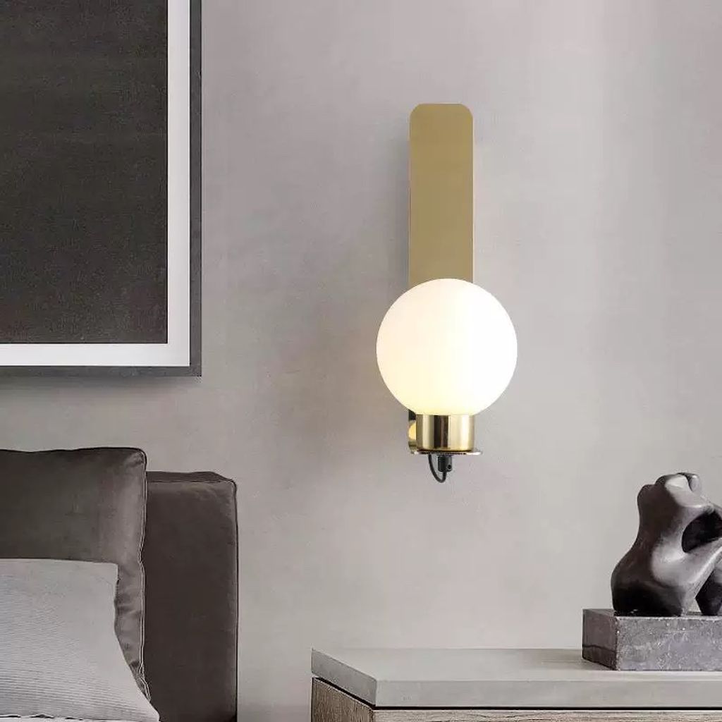 Đèn vách tường trang trí thiết kế đèn lấy cảm hứng từ phong cách Bắc Âu hiện đại, kết hợp giữa chất liệu kim loại mạ vàng ánh đồng cao cấp và chụp đèn thủy tinh mờ hình cầu, tạo nên tổng thể vừa thanh lịch vừa thời thượng. Bề mặt đế đèn được xử lý nhẵn mịn, bo góc nhẹ nhàng, mang lại cảm giác mềm mại và hài hòa khi lắp đặt trên tường.