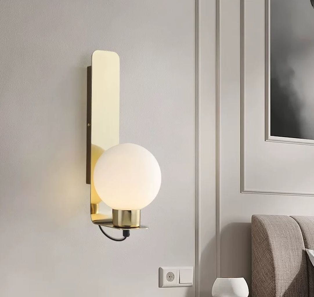 Đèn vách tường trang trí thiết kế đèn lấy cảm hứng từ phong cách Bắc Âu hiện đại, kết hợp giữa chất liệu kim loại mạ vàng ánh đồng cao cấp và chụp đèn thủy tinh mờ hình cầu, tạo nên tổng thể vừa thanh lịch vừa thời thượng. Bề mặt đế đèn được xử lý nhẵn mịn, bo góc nhẹ nhàng, mang lại cảm giác mềm mại và hài hòa khi lắp đặt trên tường.