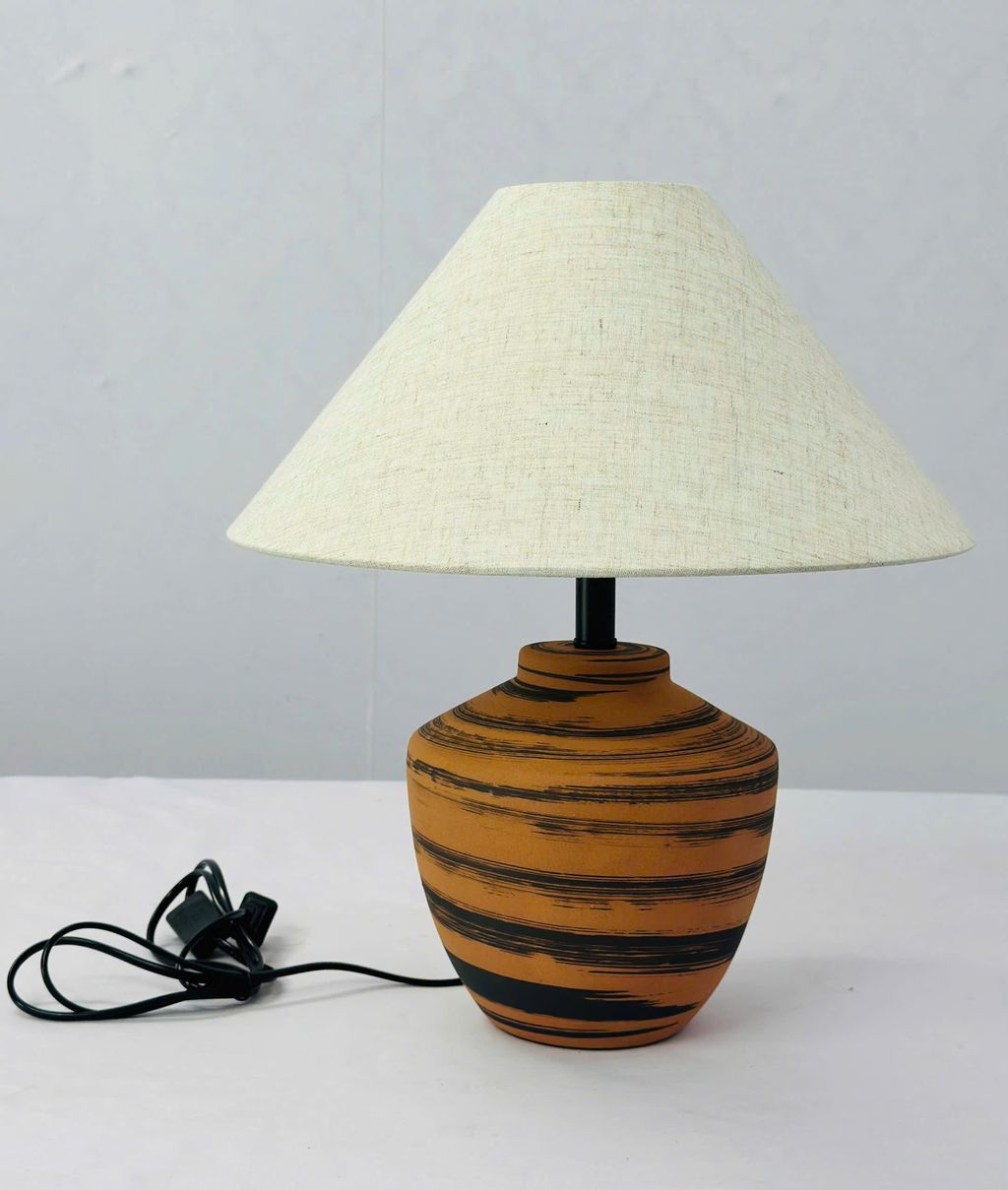 Đèn bàn vân gốm sang trọng với thân đèn được chế tác từ chất liệu gốm sứ cao cấp. Gam màu cam đất phối sọc đen tạo hiệu ứng thị giác mạnh mẽ mà vẫn giữ nét mộc mạc đặc trưng của chất liệu thủ công. Thiết kế này phù hợp với nhiều phong cách nội thất. Từ Scandinavian tối giản, phong cách Nhật trầm lắng đến không gian hiện đại đương đại.