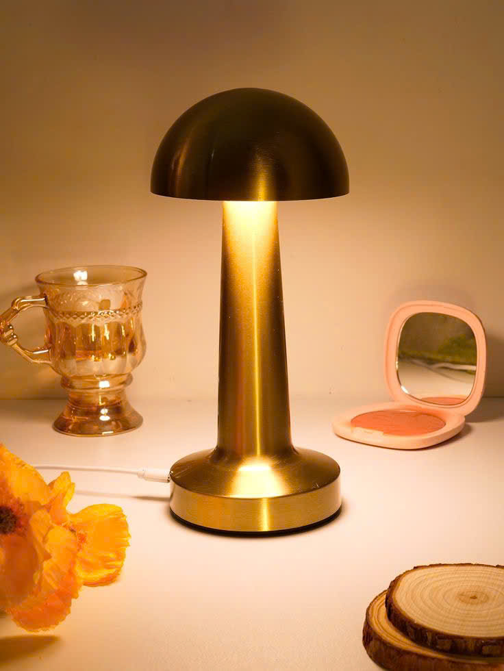 Đèn để bàn mạ vang lấy cảm hứng từ hình dáng cây nấm nhỏ xinh. Đèn để bàn nổi bật với thiết kế tối giản, gọn gàng mà vẫn tinh tế đến từng đường nét. Toàn bộ thân đèn được phủ lớp mạ vàng bóng mượt, phản chiếu ánh sáng nhẹ nhàng. Tạo cảm giác ấm áp và sang trọng cho căn phòng.