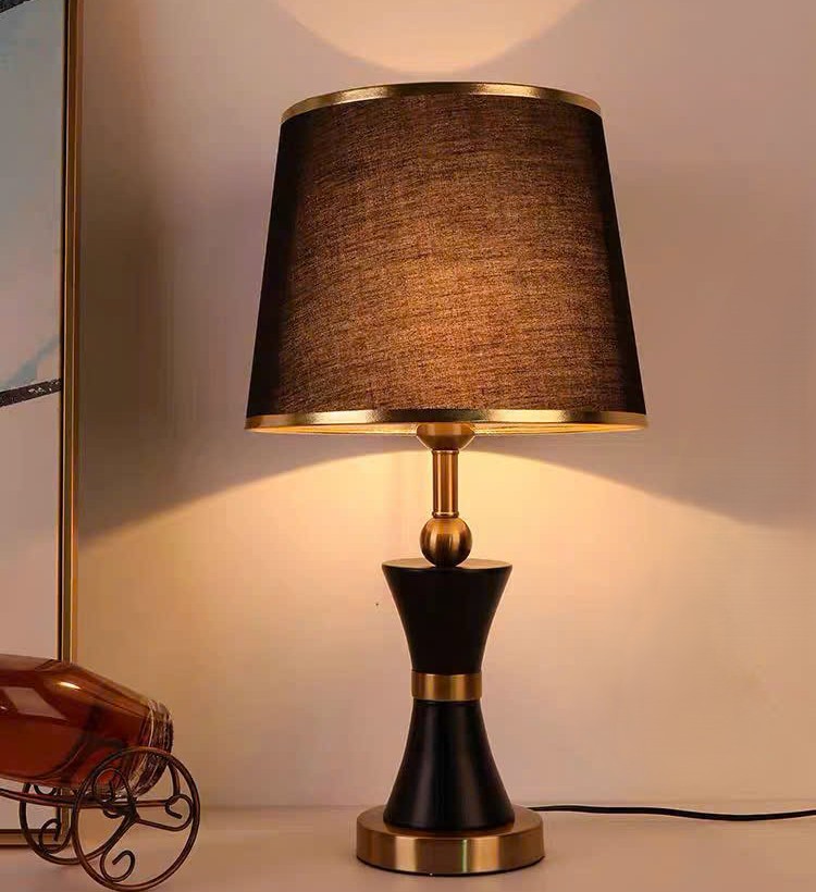 Đèn bàn Lumos Ánh Kim gây ấn tượng ngay từ cái nhìn đầu tiên với phần chụp đèn bằng vải nâu đồng mềm mại, tạo nên ánh sáng dịu nhẹ và ấm cúng. Thân đèn được chế tác từ kim loại mạ vàng cao cấp kết hợp cùng tông đen huyền bí, mang đến sự hài hòa giữa cổ điển và hiện đại. Những chi tiết bo tròn, cân đối và tinh xảo khiến chiếc đèn để bàn cổ điển này trở thành một tác phẩm nghệ thuật thực thụ.